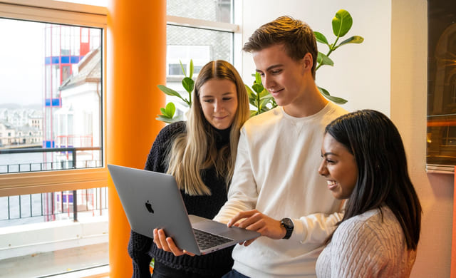 Tre elever på Akademiet kikker på Macbooken