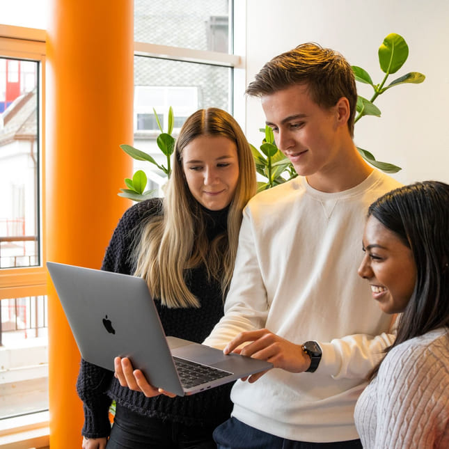 Tre elever på Akademiet kikker på Macbooken