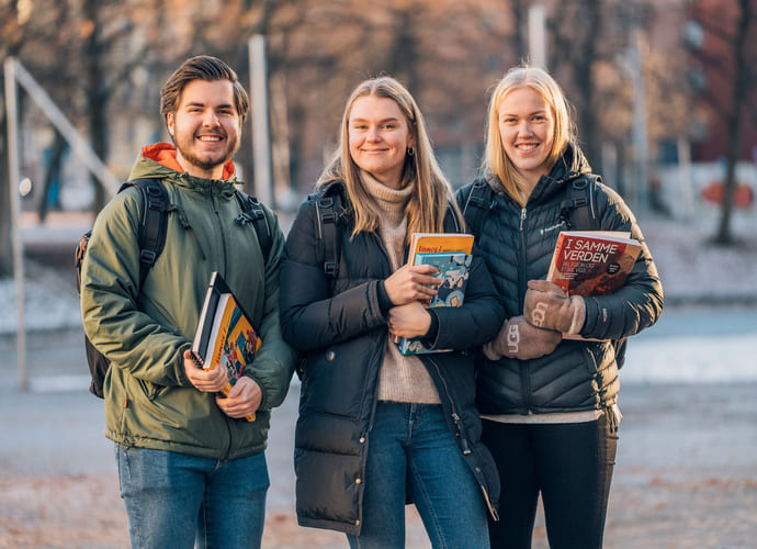 Tre privatister står utenfor skolen og holder bøker