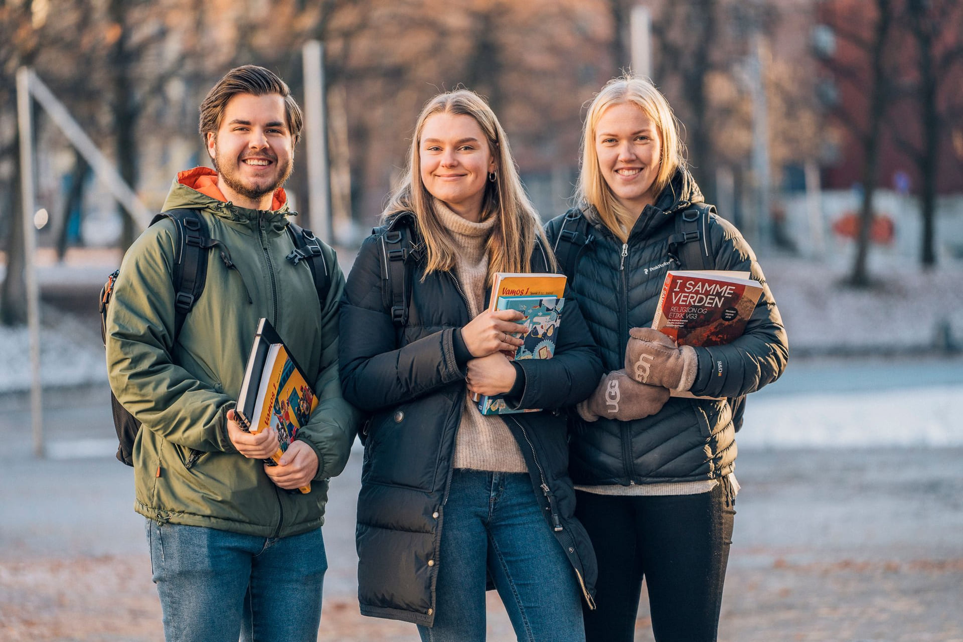 Tre elever ved Akademiet Privatistskole og Nettstudier står utendørs med bøker i hendene