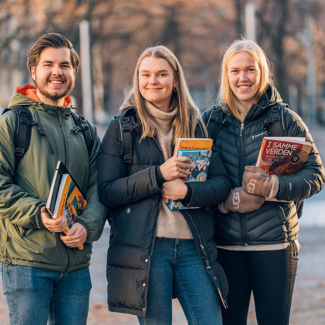 Tre elever ved Akademiet Privatistskole og Nettstudier står utendørs med bøker i hendene
