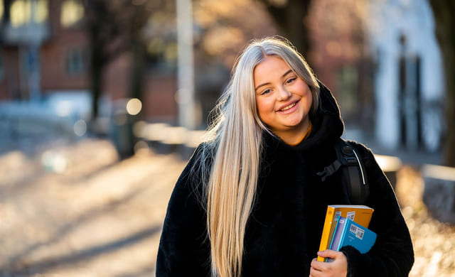 Privatist smiler og holder en lærerbok i hånden