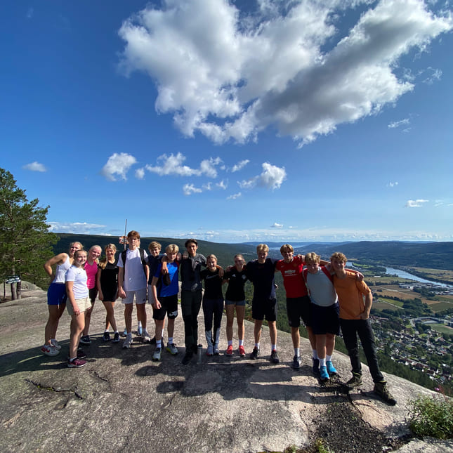 En gjeng elever fra Akademiet VGS Heltberg Drammen smiler fra toppen av et fjell