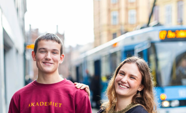 To elever på Akademiet står utenfor skolen ved trikkestoppet