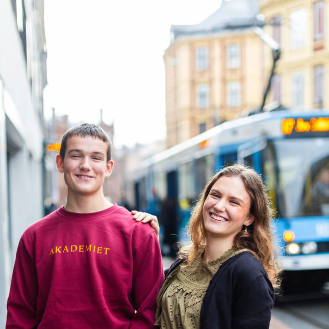 To elever på Akademiet står utenfor skolen ved trikkestoppet