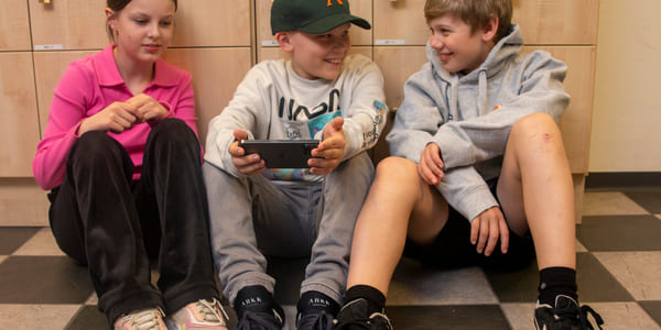 Elever på Ålesund Realfagsungdomsskole sitter på gulvet og holder på med mobil
