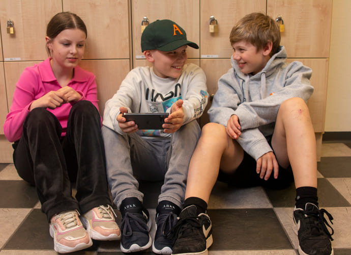 Elever på Ålesund Realfagsungdomsskole sitter på gulvet og holder på med mobil