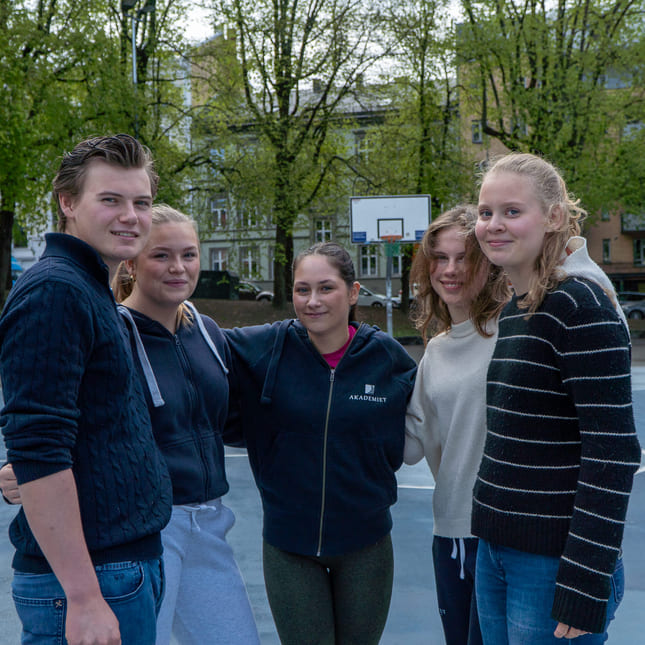 Elever på Akademiet VGS Oslo står utenfor skolen og smiler.