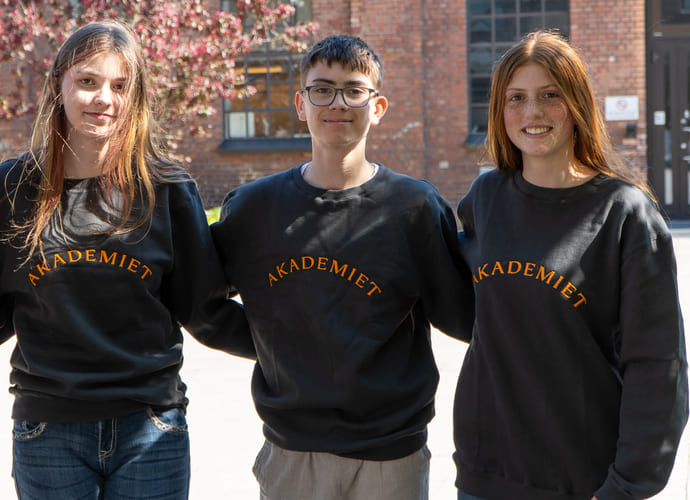 Tre elever med Akademietgenser smiler og holder rundt hverandre.