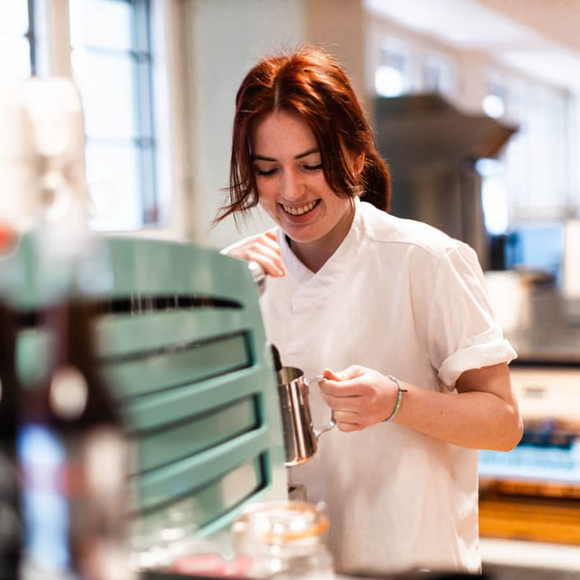 Elev på Akademiet Norsk Restaurantskole smiler mens hun lager kaffe