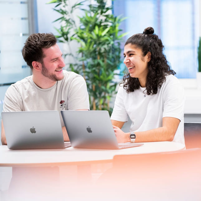 To privatister fra Akademiet Privatistskole sitter ved et bord og jobber med en MacBook