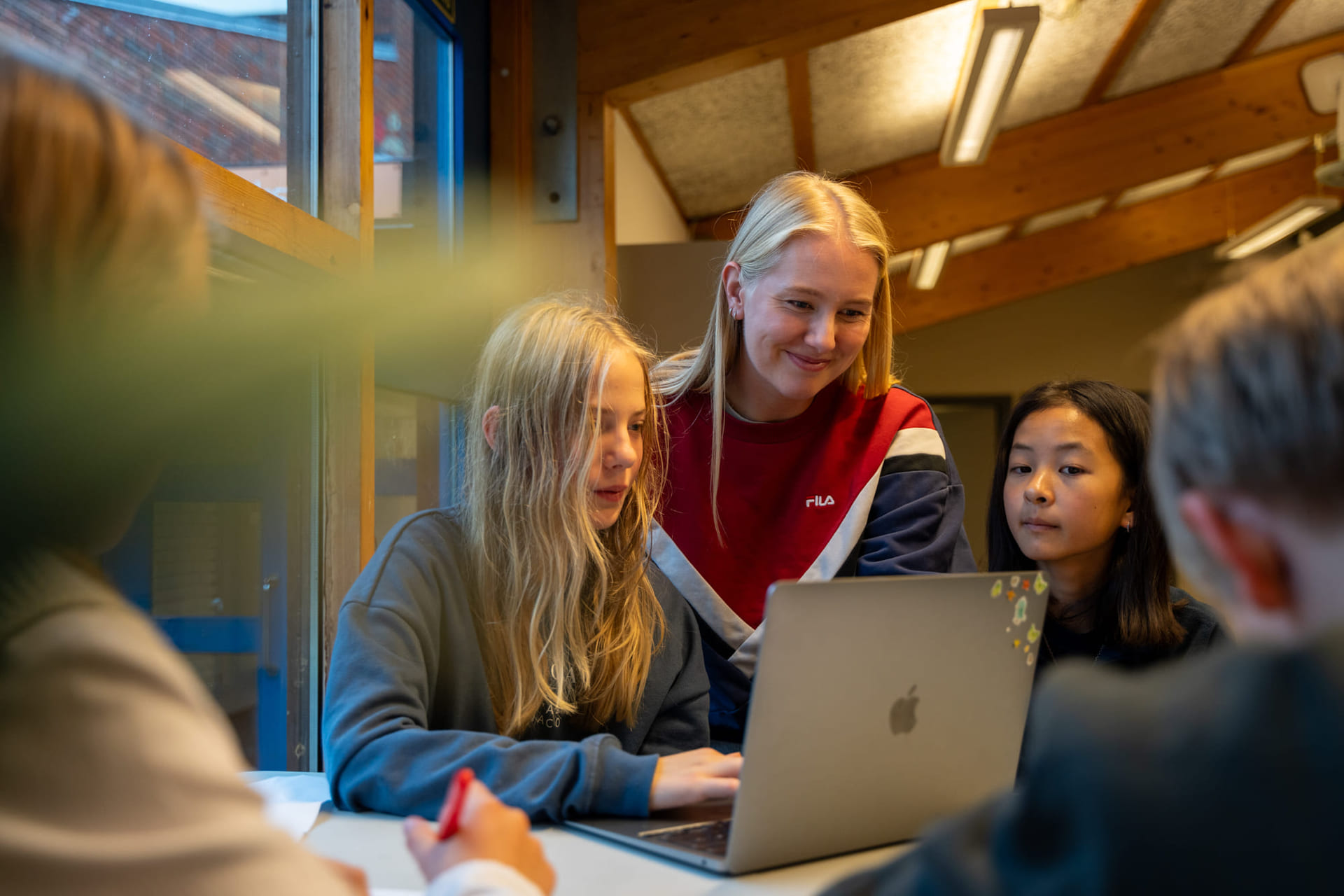 Elever og lærer snakker sammen om en oppgave på macbook.