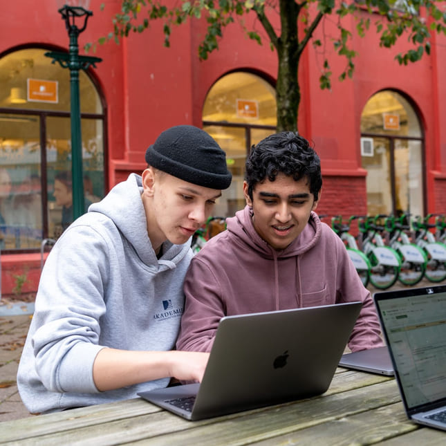 Elever på Akademiet VGS Bergen sitter utenfor skolen og jobber med fag.