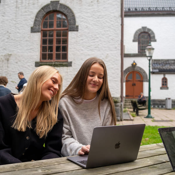 To elever sitter utenfor Akademiet VGS Bergen og jobber med skolearbeid