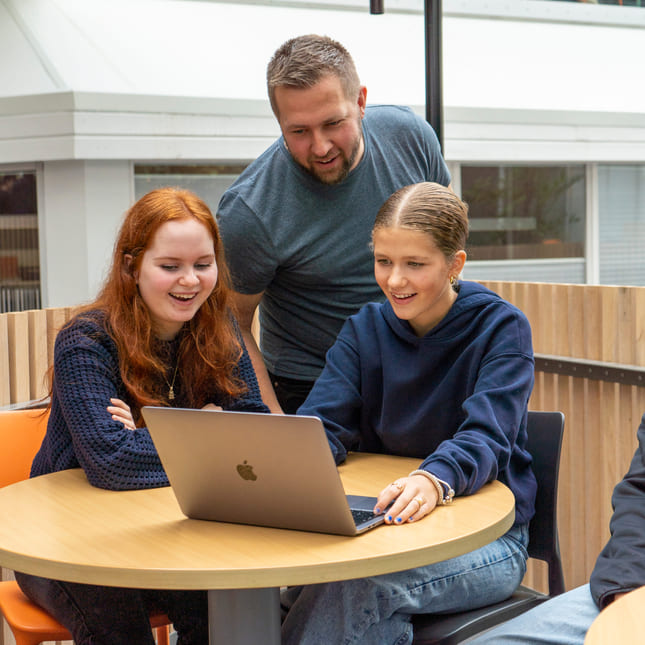 Elever og mentor kikker på mac på Akademiet VGS Sandnes