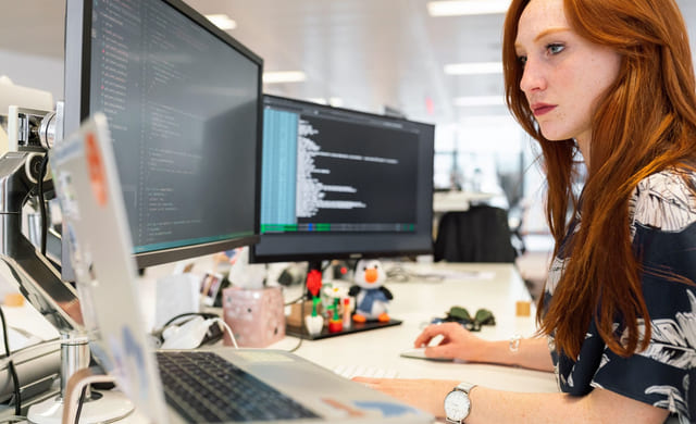 Kvinne sitter på pulten og jobber med koding