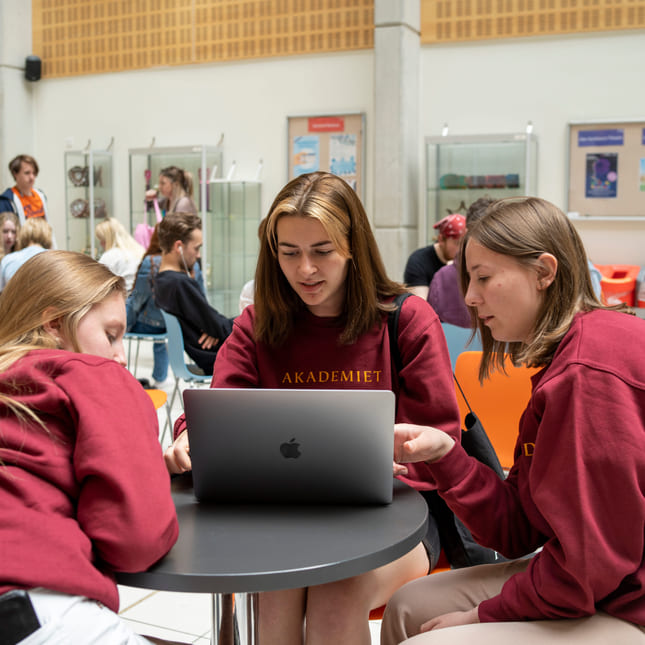 Tre elever snakker sammen rundt et bord på en skole.