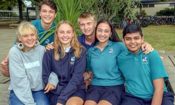 En gjeng elever smiler til kamera og holder rundt hverandre med skoleuniform i New Zealand.