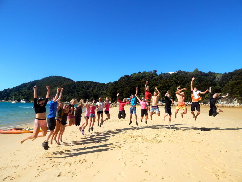 En gjeng elever hopper på stranda i new zealand
