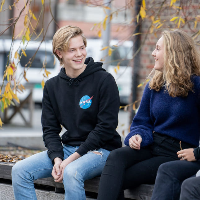 Fire elever fra Akademiet VGS Heltberg Drammen sitter på en benk