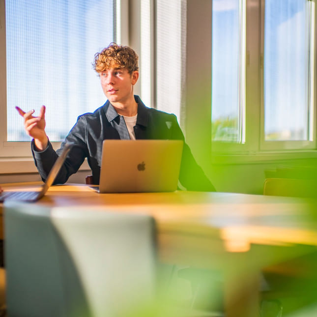 Elev peker på en annen elev mens han arbeider på macbook på akademiet vgs oslo