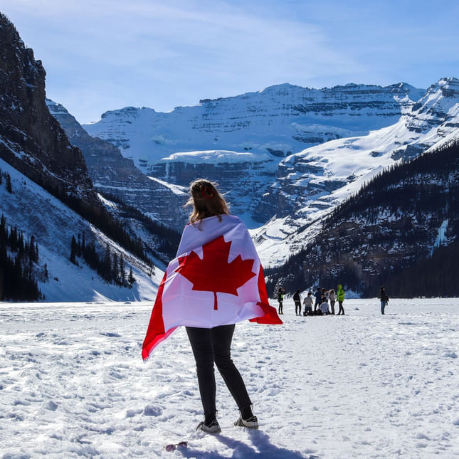 Person står i snøen med det kanadiske flagget rundt seg