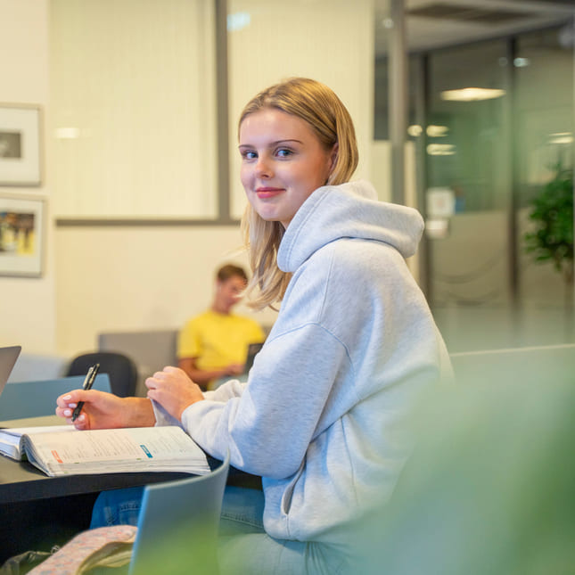 Elev på Akademiet VGS Kristiansand smiler mens hun jobber med fag.