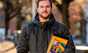 Gutt står ute med skolebok i hånden. Foto.