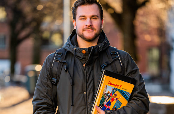 Gutt står ute med skolebok i hånden. Foto.
