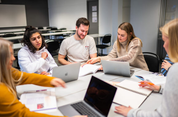 En gruppe privatister som sitter sammen og diskuterer rundt et bord med notatblokker og Mac. Foto.