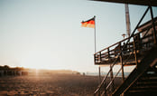 Tysk flagg som svaier i vinden på stranden i solnedgang. Foto.r