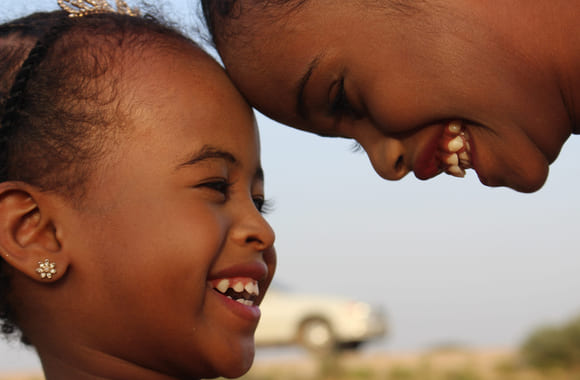Et barn og en ungdom i Somalia, med hodene mot hverandre som smiler og ler. Foto.