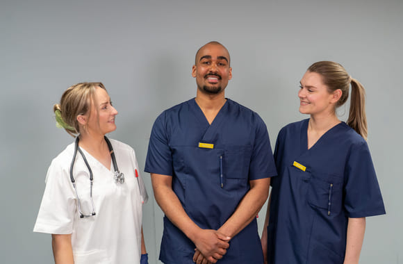 Tre medisinstudenter som står og smiler sammen i gang på sykehus. Foto.