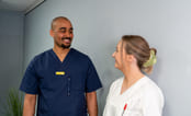Helseassistent og legestudent snakker sammen i gangen på sykehuse. Foto.