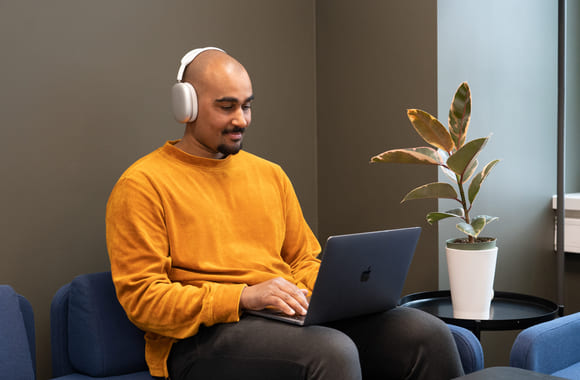 Privatist som jobber på Mac i sofa med headset. Foto.