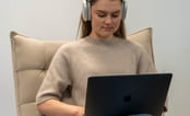 Jente som sitter i stol med Mac og headset. Foto.