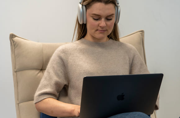 Jente som sitter i stol med Mac og headset. Foto.