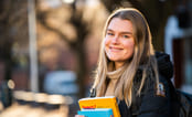 Jente smiler ute med skolebøker i hendene. Foto.
