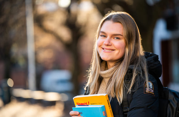 Jente smiler ute med skolebøker i hendene. Foto.