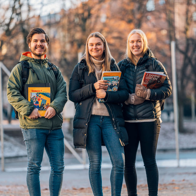 Tre privatister står utendørs med bøker og Mac fra Akademiet Privatistskole