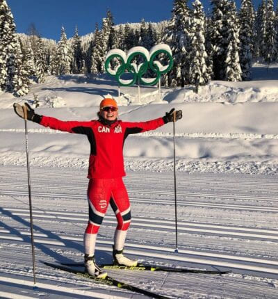 Person i skidress smiiler med OL-logoen bak i Whistler i Canada