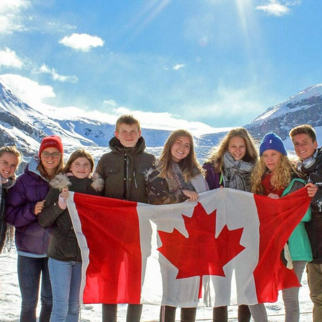 Elever holder opp det kanadiske flagget i vinteromgivelser og sol i Canada.