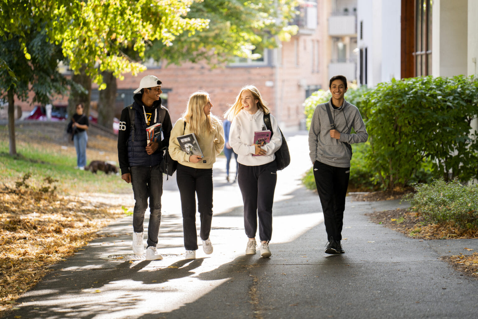 Fire elever på Akademiet VGS Heltberg Bislett går langs en vei med grønne trær rundt seg