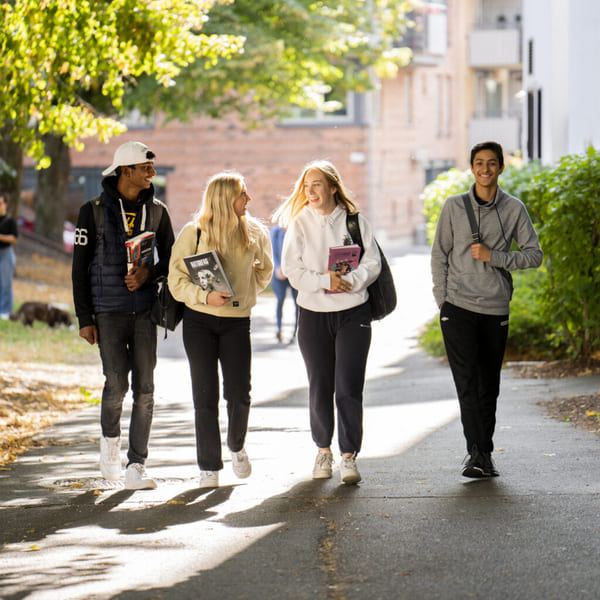 Fire elever på Akademiet VGS Heltberg Bislett går langs en vei med grønne trær rundt seg