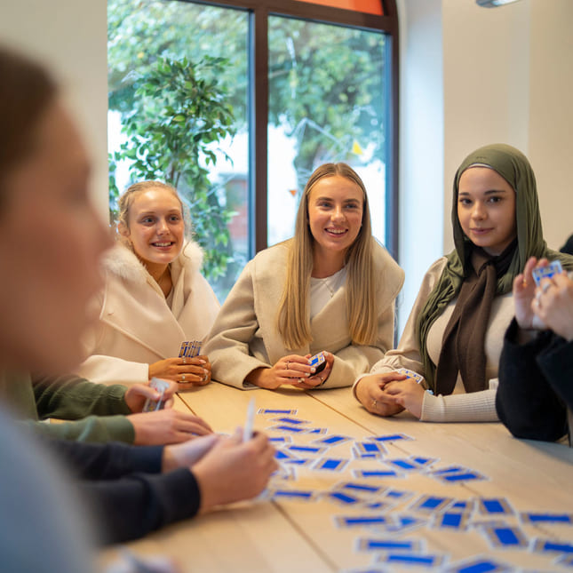 Elever spiller kort sammen rundt et bord på Akademiet VGS Bergen