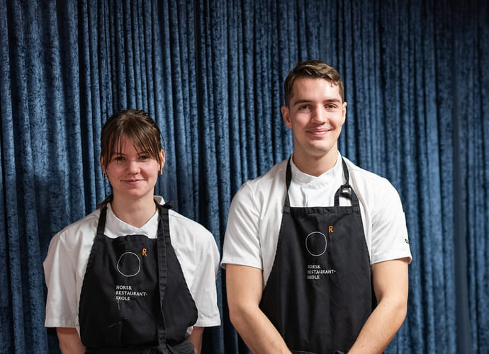 To elever på akademiet norsk restaurantskole poserer foran et dekket bord.