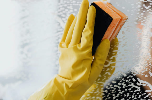 Person med gule hansker vasker et speil.