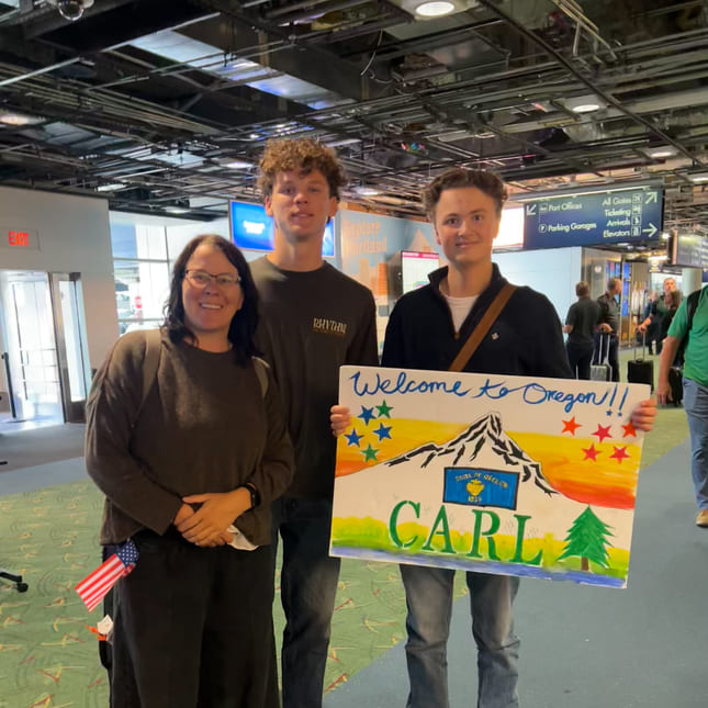 Vertsfamilien til Carl tar imot han på flyplassen og har laget et skilt hvor det står "velkommen Carl".