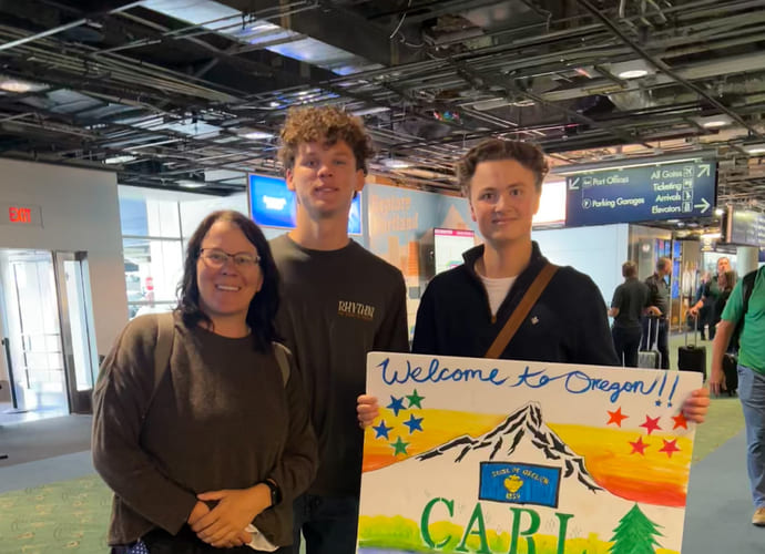 Vertsfamilien til Carl tar imot han på flyplassen og har laget et skilt hvor det står "velkommen Carl".