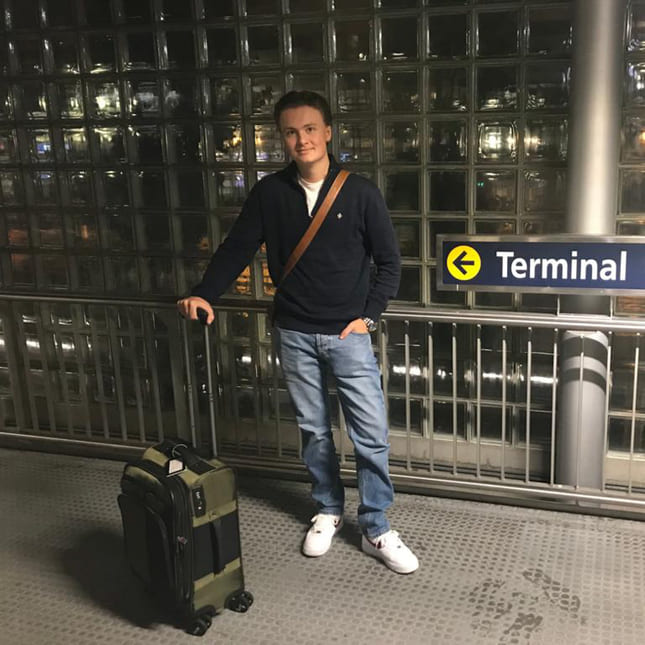 Carl står på flyplassen i Norge med kofferten, klar for å reise.
